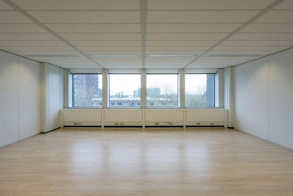 Empty office space with large windows in the Laan van Kronenburg building.